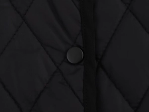 Close-up of diamond quilted fabric featuring a matte black snap button on winter jacket