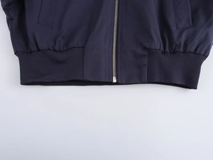 Detail of navy bomber jacket featuring silver zipper, ribbed hem, and flap pockets