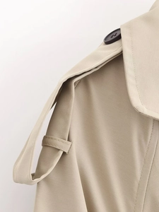 Dettaglio della spallina di un trench kaki con bottone scuro e trama in twill