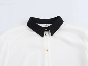Dettaglio del colletto a contrasto con bottone dorato su camicia bianca a maniche lunghe