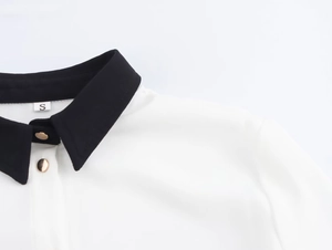 Dettaglio del colletto di una camicia da donna con contrasto nero e bottoni dorati