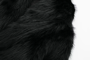 Close-up of thick black faux fur fabric with glossy texture and soft high-density fibers
