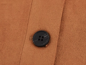 Close-up of caramel suede texture with a black round four-hole button and stitching details