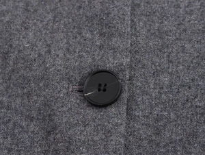 Macro shot of grey wool blend fabric and a black four-hole resin button on a blazer