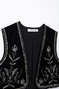 Dettaglio di ricamo floreale in oro e argento con paillettes su gilet di velluto nero