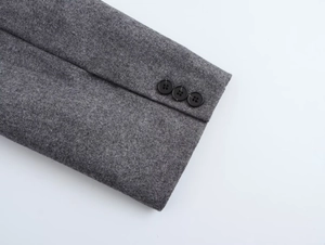 Close-up of three polished buttons on dark grey wool blazer sleeves with fine texture