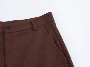 Dettaglio dei pantaloni marrone scuro con chiusura a bottone, passanti e tasche