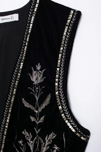 Dettaglio macro del ricamo floreale argento su un gilet di velluto nero aperto