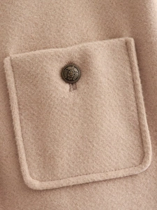 Detail showing vintage metal button and pocket on camel wool texture winter coat