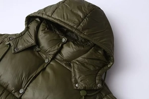Close-up of olive green puffer jacket featuring metallic snaps and adjustable hood cords