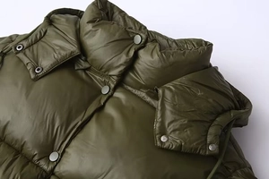 Detail of army green puffer jacket showing high collar hood and silver snap buttons