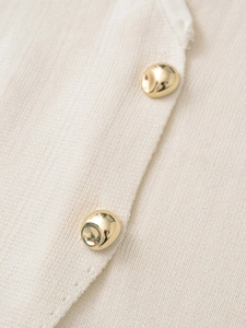 Détail de la maille blanc cassé avec deux boutons métalliques dorés de forme irrégulière