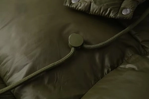 Detail of olive green puffer jacket featuring metallic snaps and adjustable hood drawstrings
