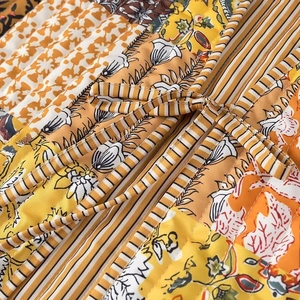 Detail of quilted women vest showing colorful floral patterns and striped tie closure