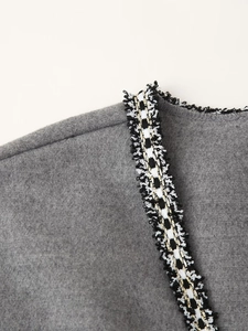 Close-up of gray wool coat with black, white and gold woven tape and frayed edges