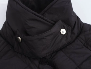 Detail of black quilted jacket featuring high collar with silver metal snap buttons