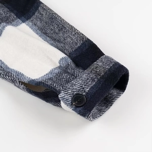 Detail van de manchet van een geruit wollen jasje met blauw-wit patroon en knoop