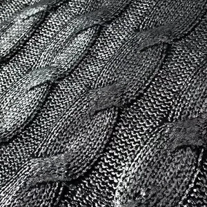 Macro view of cable knit sweater fabric with metallic gold foil texture and shimmering finish