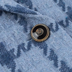 Close-up of blue tweed jacket fabric and a vintage gold button with black enamel detail