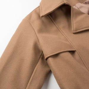 Detailed close-up of camel wool coat lapel and layered shoulder tailoring with fine stitching