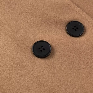 Detail of warm camel wool coat featuring premium texture and black four-hole buttons