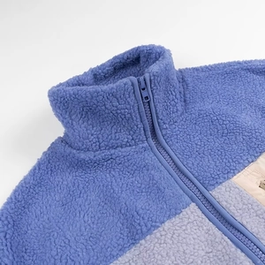Detailed view of the fuzzy fleece texture on a blue and gray patchwork jacket with zipper