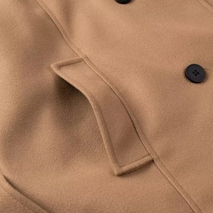 Detail of camel wool coat showing texture, side flap pocket and black button finish