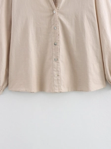 Detail of linen texture and shell buttons on a beige long-sleeved V-neck shirt