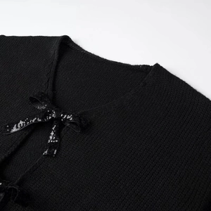 Close-up of black knit cardigan featuring a sequined bow tie detail at the neckline