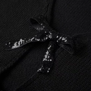 Detail of black knit cardigan featuring a bow accent with sparkling silver sequins