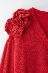 Dettaglio ravvicinato di un maglione rosso con una grande decorazione a fiore in maglia 3D