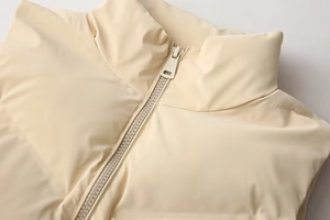Detail view of the standing collar and smooth resin zipper on this beige padded vest
