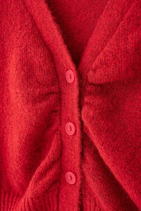 Vista macro di un cardigan rosso a maglia con scollo a V, volant e bottoni tondi abbinati