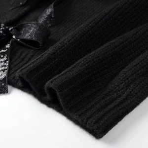 Detail of black ribbed knit cardigan featuring a sparkling sequin bow decoration