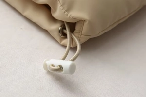 Detail of drawstring toggle and metal eyelet on light beige quilted padded vest