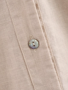 Macro detail of natural linen fabric texture and iridescent engraved button on beige shirt