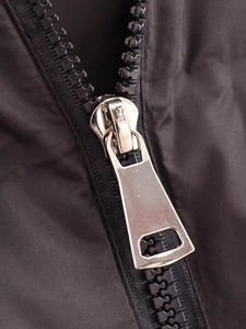 Detailed macro view of a bright silver metal zipper puller on a black quilted vest