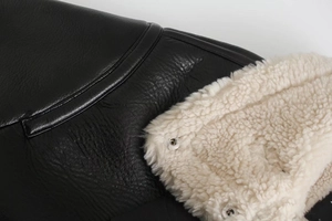 Detail of black pebbled leather jacket with off-white fleece lining and silver snap buttons