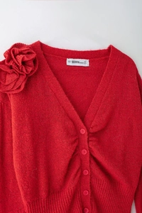 Dettaglio cardigan rosso in maglia con scollo a V, fiore 3D e chiusura con bottoni