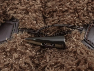 Detail of a toggled horn button on a brown faux shearling coat with leather trim accents