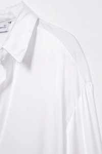 Détail du col à revers et de la texture satinée sur cette chemise blanche à manches longues