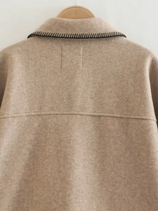 Detail of camel wool coat featuring black whipstitch embroidery on the collar neckline