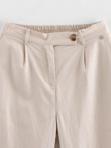 Detail view of beige linen trousers with elastic waist and metal petal pendant