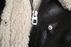 Detailed macro view of silver zipper on black faux leather jacket with plush shearling lining