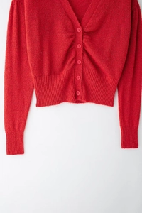 Dettaglio del cardigan in maglia rossa con scollo a V, trama lavorata e bottoni tondi