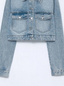 Detail of light blue denim jacket showing metal buttons and symmetrical chest pockets