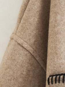 Detail of camel wool coat with decorative black whipstitch seams and textured wool fabric
