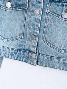Detailed close-up of light blue denim jacket texture with high-quality metal buttons