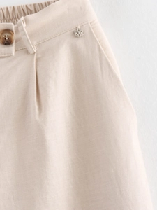 Detail of linen trousers with elastic waist, wooden button and silver flower ornament