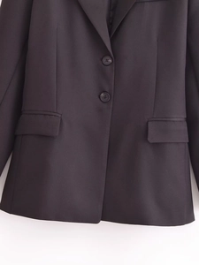 Detail of a black slim-fit blazer with two-button closure and flap pockets on a white background